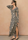 Woman wearing a long, patterned dress against a beige background