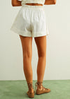Person wearing white shorts and brown shoes on a green floor with a light gray wall background