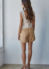 Woman wearing a striped sleeveless top and beige shorts against a plain wall.