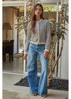 A woman stands in a modern home entryway wearing a cream and navy blue horizontally striped knit cardigan with ruffled trim, paired with wide-leg blue jeans.