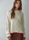 Woman wearing a cream knitted sweater with red trim against a plain background