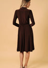 A woman modeling a dark brown long-sleeve midi dress from the back, standing against a solid beige studio background.
