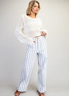Woman wearing a white crochet top and striped pants on a plain background