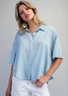 Woman wearing a light blue denim shirt and white pants on a gray background