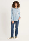 Woman wearing a light blue denim shirt and dark blue jeans on a white background