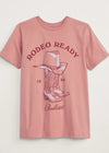 Pink t-shirt with 'Rodeo Ready' graphic and cowboy boots on a light beige background