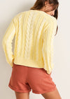 Woman wearing a yellow cable knit cardigan and red shorts against a plain background