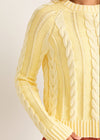 Close-up of a yellow cable knit sweater on a plain background