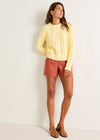 Woman wearing a yellow sweater and red shorts against a white background