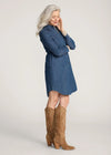 Woman wearing a blue denim dress with brown knee-high boots on a plain background
