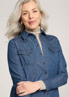 Woman wearing a blue denim shirt over a beige turtleneck against a plain background