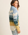 Woman wearing a colorful sweater with nature-themed design on a plain background