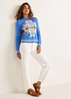 Woman wearing a blue sweater with a pattern, white pants, and brown shoes on a white background