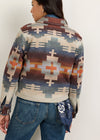 A woman shown from the back wearing a cropped long-sleeve knit sweater with a Southwestern geometric pattern in blue, rust orange, beige, and brown, paired with blue jeans.