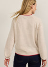 A woman shown from the back wearing a cream-colored knit sweater with red trim details on the collar, cuffs, and hem, paired with dark blue jeans against a plain light background.
