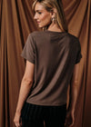 A woman wearing a short-sleeve crewneck t-shirt in a dark brown color, shown from the back against a draped brown fabric backdrop.