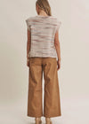A woman shown from the back wearing a cream knit sweater vest with brown and pink horizontal streaks, paired with wide-leg tan pants and beige heels, against a solid light beige background.