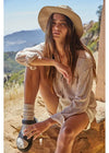 Woman sitting outdoors wearing a straw hat and striped shirt with mountains in the background