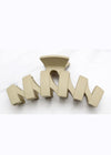 Beige hair clip with 'M' design on a white background