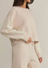 Person wearing a beige sweater and pants against a plain background