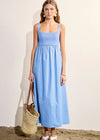 Woman wearing a blue dress holding a straw bag on a beach.
