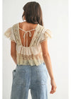 Woman wearing a lace top with open back and light blue jeans on a white background