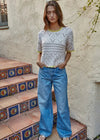 Woman wearing a patterned top and blue jeans standing on decorative steps.