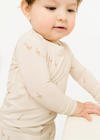 Baby wearing a beige long-sleeve shirt with small patterns on a white background