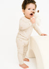 Baby in a white outfit holding a plush toy on a white background