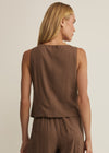 Woman wearing a brown sleeveless top and pants against a beige background