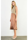 A woman models a sleeveless midi dress with a beige knit mock-neck bodice and a bronze satin skirt, paired with beige pointed-toe heels against a plain white studio background.