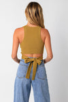 Woman wearing a mustard yellow sleeveless top and blue jeans with a belt on a white background