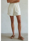 Person wearing white shorts and brown sandals against a plain background