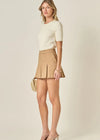 Woman wearing a cream top and beige skirt on a plain background