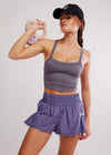 Woman in purple athletic wear lifting a pink kettlebell against a light gray background