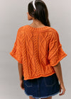Person wearing an orange knitted poncho against a gray background