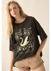 A woman wearing a black oversized t-shirt with a white swan and leaf graphic, paired with tan denim shorts, set against a plain beige background.