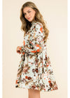 A woman modeling a long-sleeve floral dress with a tie waist, shown from a three-quarter back angle against a solid light beige background.