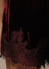 Close-up of a dark burgundy velvet garment with a wide matching lace trim and fringe, worn on a person's lower torso or skirt area.