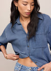 Woman wearing a blue denim shirt and jeans against a neutral background