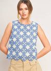 Woman wearing a blue and white patterned sleeveless top with beige pants on a plain background