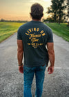 Man walking on a road with a t-shirt reading 'Living on Farmer Time' in a rural setting.