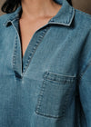 Close-up of a person wearing a blue denim shirt-jacket with a pointed collar, split neckline, and a chest pocket.