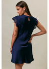A woman modeling a navy blue satin mini dress from the back, featuring lace cap sleeves and a keyhole back cutout, set against a plain beige studio background.