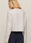 Person wearing a light gray sweater and dark pants on a beige background