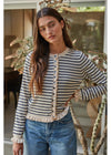 A woman wearing a cream and navy blue horizontally striped cardigan with a decorative button placket and ruffled trim, paired with blue jeans.