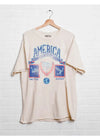 Beige t-shirt with graphic design on a hanger against a white brick wall
