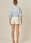 Person wearing a light blue striped shirt and white shorts on a beige background