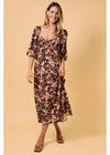 A woman modeling a floral midi dress with three-quarter sleeves and a V-neckline, set against a solid beige studio background.