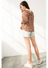 Woman wearing a patterned blouse and denim shorts against a white background
